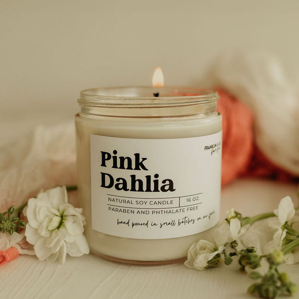 Pink Dahlia candle with a label on a surface with flowers