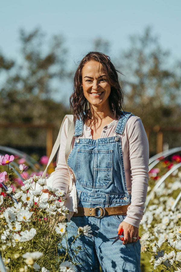 Cory Franklin in overalls with cosmos tucked in her pocket, standing in our zone 3 flower field at Charlie Lake BC