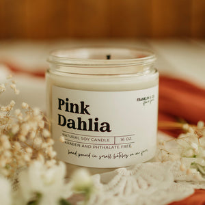 Candle labeled 'Pink Dahlia' on a decorative surface with flowers and doily.