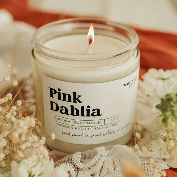 Pink Dahlia candle with a label on a decorative surface with flowers and lace.
