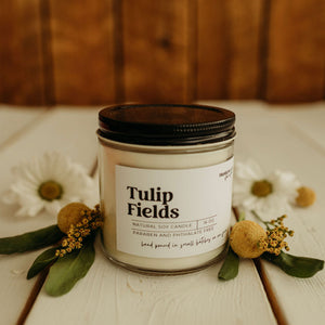 Candle jar labeled 'Tulip Fields' with flowers on a wooden surface