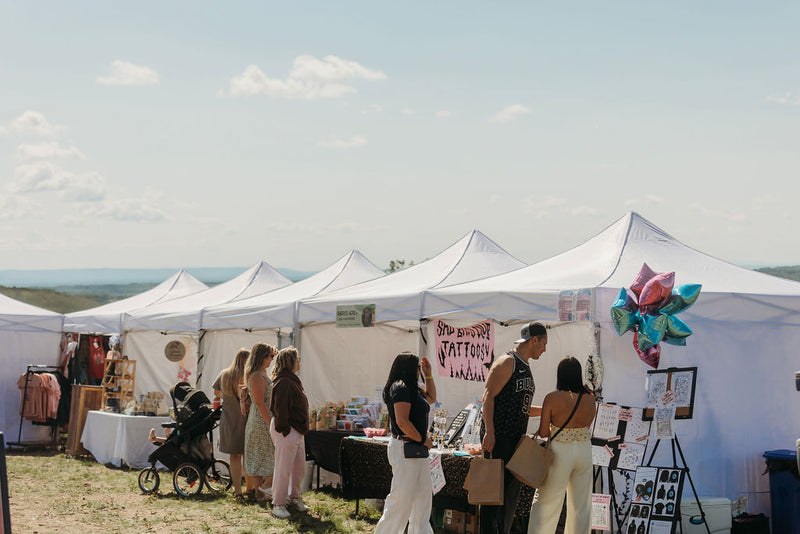 Shoppers visiting white vendor tents on the hilltop at Summer in Bloom, Charlie Lake BC