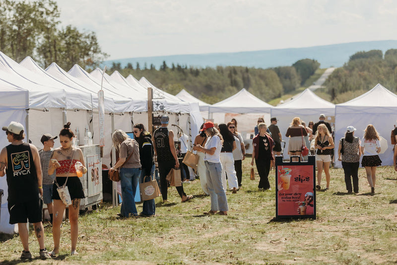 Crowd of shoppers walking between rows of white vendor tents at Summer in Bloom, Charlie Lake BC