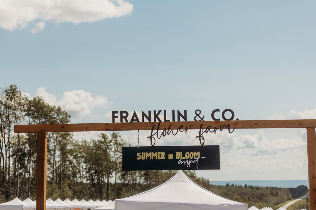 Franklin & Co. Flower Farm and Summer in Bloom sign on a wooden arch over the market