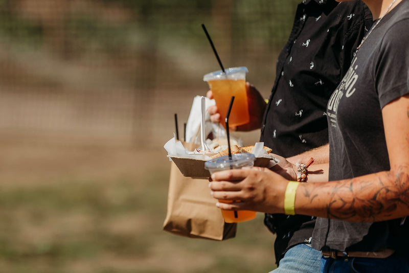 Guests carrying iced drinks and a takeout bag at Summer in Bloom market
