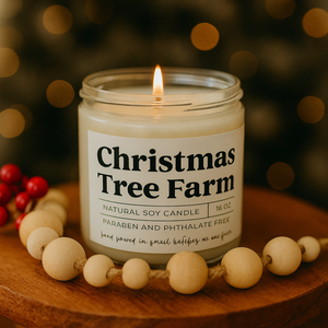 Candle labeled 'Christmas Tree Farm' on a wooden surface with blurred lights in the background